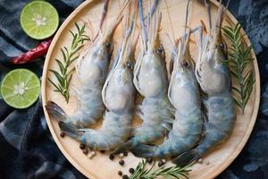 fresh shrimps prawns seafood shelfish with herb and spices chilli pepper lemon lime rosemary, raw shrimp on plate wooden background for cooking food photo