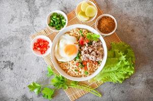noodles bowl with boiled egg minced pork vegetable spring onion lemon lime lettuce celery and chili on table food , instant noodles cooking tasty eating with bowl noodle soup photo