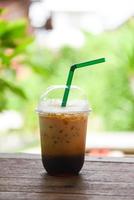 Iced coffee latte in plastic cup on wooden table and nature green background - iced drinks photo