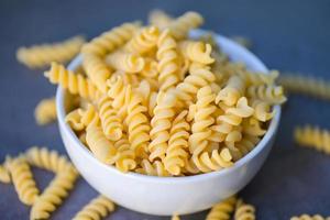 Raw pasta macaroni on white bowl, close up raw macaroni spiral pasta uncooked delicious fusilli pasta for cooking food photo