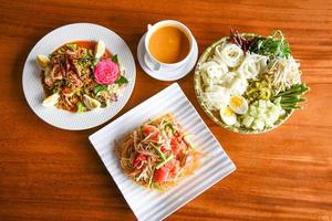 Asian Thai food top view with Thai rice noodles , curry Papaya salad , shrimp salad food served on wooden table setting plate photo