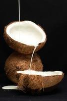 concepto de fruta tropical, leche de coco vertida en mitades de coco fresco sobre fondo negro