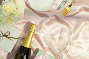 Festive table set concept, Champagne with glass and peony with gift box on table cloth for diner photo