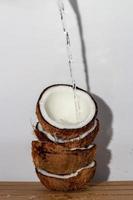 concepto de fruta tropical, agua de coco vertida en mitades de coco fresco apiladas sobre fondo de madera