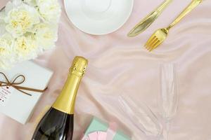 Festive table set concept, Champagne with glass and peony with gift box on table cloth for diner photo