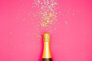 Festive party concept, Champagne bottle with confetti glitter colorful stars on pink background photo