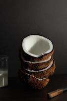 concepto de fruta tropical, mitades de coco fresco apiladas con leche de coco sobre madera y fondo negro