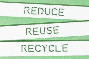 Reduce Reuse Recycle message on cut out paper strips on green background photo