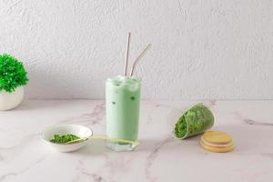 A tall glass of organic green tea matcha latte with eco-friendly metal straw stands on a marble table. scattered tea powder from a jar. photo