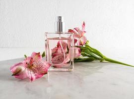 a bottle of perfume on a marble slab against the background of a textured wall and a pink flower. advertising concept of women's parffumeria. photo