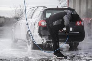 el auto en el lavado de autos está cubierto de espuma, se lava a presión con un chorro de agua foto