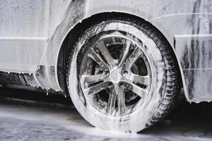 el auto en el lavado de autos está cubierto de espuma, se lava a presión con un chorro de agua foto