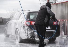 el auto en el lavado de autos está cubierto de espuma, se lava a presión con un chorro de agua foto
