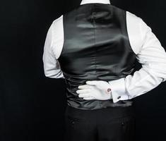 retrato de mayordomo o camarero con guantes blancos y chaleco negro de pie con la mano detrás de la espalda. concepto elegante de la industria hotelera. foto