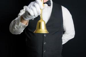 retrato de mayordomo o camarero con chaleco negro y guantes blancos sosteniendo una campana dorada. concepto de industria de servicios y cortesía profesional. anillo de servicio. foto