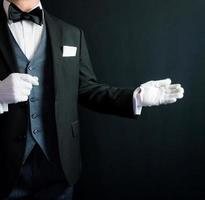 retrato de mayordomo con gesto de bienvenida en traje formal y guantes blancos. Industria de servicios y cortesía profesional. foto