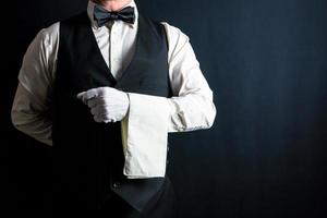 retrato de mayordomo o camarero con chaleco negro y guantes blancos y servilleta doblada sobre el brazo. Industria de servicios y hostelería profesional. foto