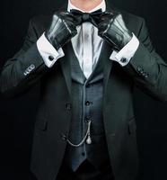 retrato de hombre con atuendo formal oscuro y guantes de cuero alisando su corbata de moño. estilo vintage y moda retro. foto