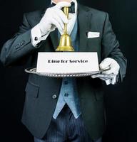 Portrait of Butler in Dark Formal Suit and White Gloves Holding Bell and Sign. Ring for Service. Concept of Professional Hospitality. photo