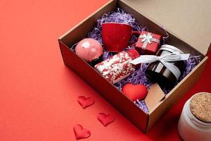 Seasonal gift box for valentine day with candle, red cup and heart shape sweets on red background photo