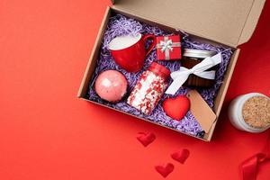 Seasonal gift box for valentine day with candle, red cup and heart shape sweets on red background