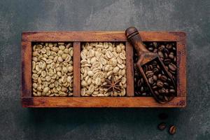 Green and brown unroasted and dark roasted coffee beans in wooden box with scoops setup on dark concrete background. photo