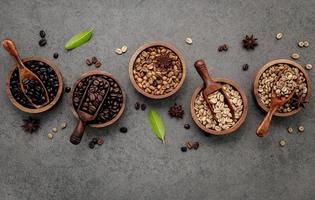 Green and brown unroasted and dark roasted coffee beans in wooden bowl with spoons set up on dark concrete background. photo