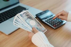 Woman hand counting Japanese Yen banknote with calculator. Thousand Yen money. Japan cash, Tax, Recession Economy, Inflation, Investment, finance, salary and payment concepts photo