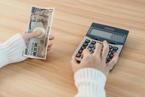 mano de mujer contando billetes de yen japonés con calculadora. dinero de mil yenes. Japón efectivo, impuestos, economía de recesión, inflación, inversión, finanzas, ahorro, salarios y conceptos de pago foto