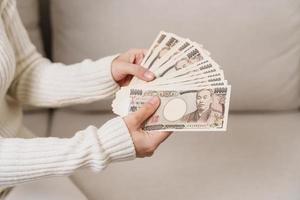 mano de mujer sosteniendo la pila de billetes de yen japonés. dinero de mil yenes. conceptos de pago en efectivo, impuestos, economía de recesión, inflación, inversión, finanzas y compras de japón foto