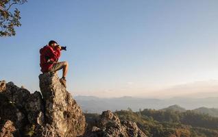 hombre sosteniendo una cámara en sus manos y haciendo fotos de las montañas durante la mañana de otoño, conceptos de senderismo y turismo