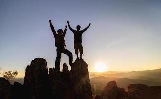 silueta de trabajo en equipo de dos hombres excursionistas ayudándose unos a otros en la parte superior del equipo de montañismo. trabajo en equipo amistad caminatas ayudarse unos a otros confianza asistencia silueta en las montañas, amanecer. foto