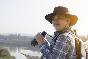 Asian boy is using binoculars to do the birds' watching in tropical forest during summer camp, idea for learning creatures and wildlife animals and insects outside the classroom. photo