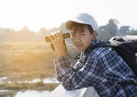 un niño asiático está usando binoculares para observar aves en el bosque tropical durante el campamento de verano, idea para aprender criaturas y animales salvajes e insectos fuera del aula. foto