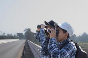 Asian boys are using binoculars to do the birds' watching in tropical forest during summer camp, idea for learning creatures and wildlife animals and insects outside the classroom. photo