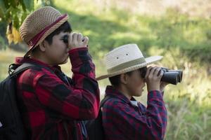 los niños asiáticos están usando binoculares para observar aves en el bosque tropical durante el campamento de verano, idea para aprender criaturas y animales salvajes e insectos fuera del aula. foto