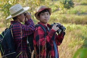 Asian boys are using binoculars to do the birds' watching in tropical forest during summer camp, idea for learning creatures and wildlife animals and insects outside the classroom. photo