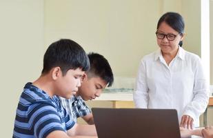 young asian teenagers and teacher, they are in class, students doing worksheet and listening to her advices about school project, adult helps kids to do school project concept. photo