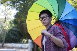 Portrait young asian boy wears rainbow wristband and holding rainbow umbrella on street, concept for being assertive in presenting your true LGBT identity to today's society is accepted by society. photo