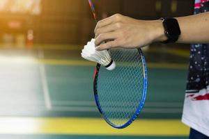 Badminton player holds white cream shuttlecock and racket in front of the net before serving it to another side of the court, soft and selective focus on shuttlecock. photo