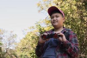 Asian boys are using binoculars to do the birds' watching in tropical forest during summer camp, idea for learning creatures and wildlife animals and insects outside the classroom. photo