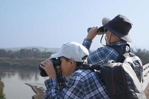 Asian boys are using binoculars to do the birds' watching in tropical forest during summer camp, idea for learning creatures and wildlife animals and insects outside the classroom. photo