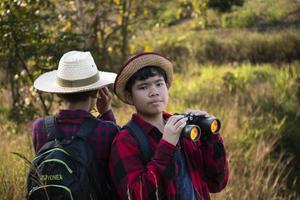 Asian boys are using binoculars to do the birds' watching in tropical forest during summer camp, idea for learning creatures and wildlife animals and insects outside the classroom. photo