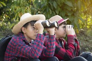 los niños asiáticos están usando binoculares para observar aves en el bosque tropical durante el campamento de verano, idea para aprender criaturas y animales salvajes e insectos fuera del aula. foto