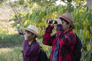 los niños asiáticos están usando binoculares para observar aves en el bosque tropical durante el campamento de verano, idea para aprender criaturas y animales salvajes e insectos fuera del aula. foto