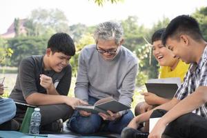 An elderly asian male is spending his spare time explaining the contents of the lesson and happily helping his two grandsons with their homework and school projects in his backyard, soft focus. photo