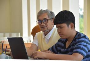 Asian eldery teacher and young teenagers surrounding inside the room to consult and to do the school project work, eldery teacher helps kids to reslove problems and advices them to get a good grade. photo