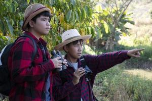 Asian boys are using binoculars to do the birds' watching in tropical forest during summer camp, idea for learning creatures and wildlife animals and insects outside the classroom. photo