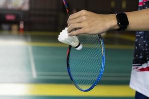 Badminton player holds white cream shuttlecock and racket in front of the net before serving it to another side of the court, soft and selective focus on shuttlecock. photo