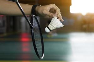 Badminton player holds white cream shuttlecock and racket in front of the net before serving it to another side of the court, soft and selective focus on shuttlecock. photo